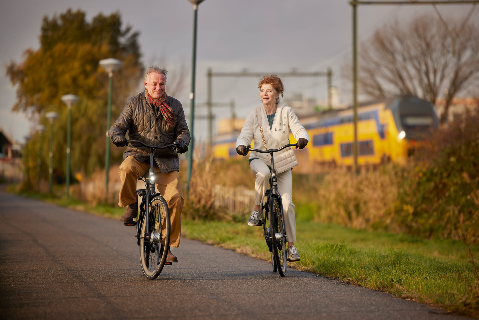 Man en vrouw fietsen naast elkaar, achter hen zien we een trein voorbijrijden