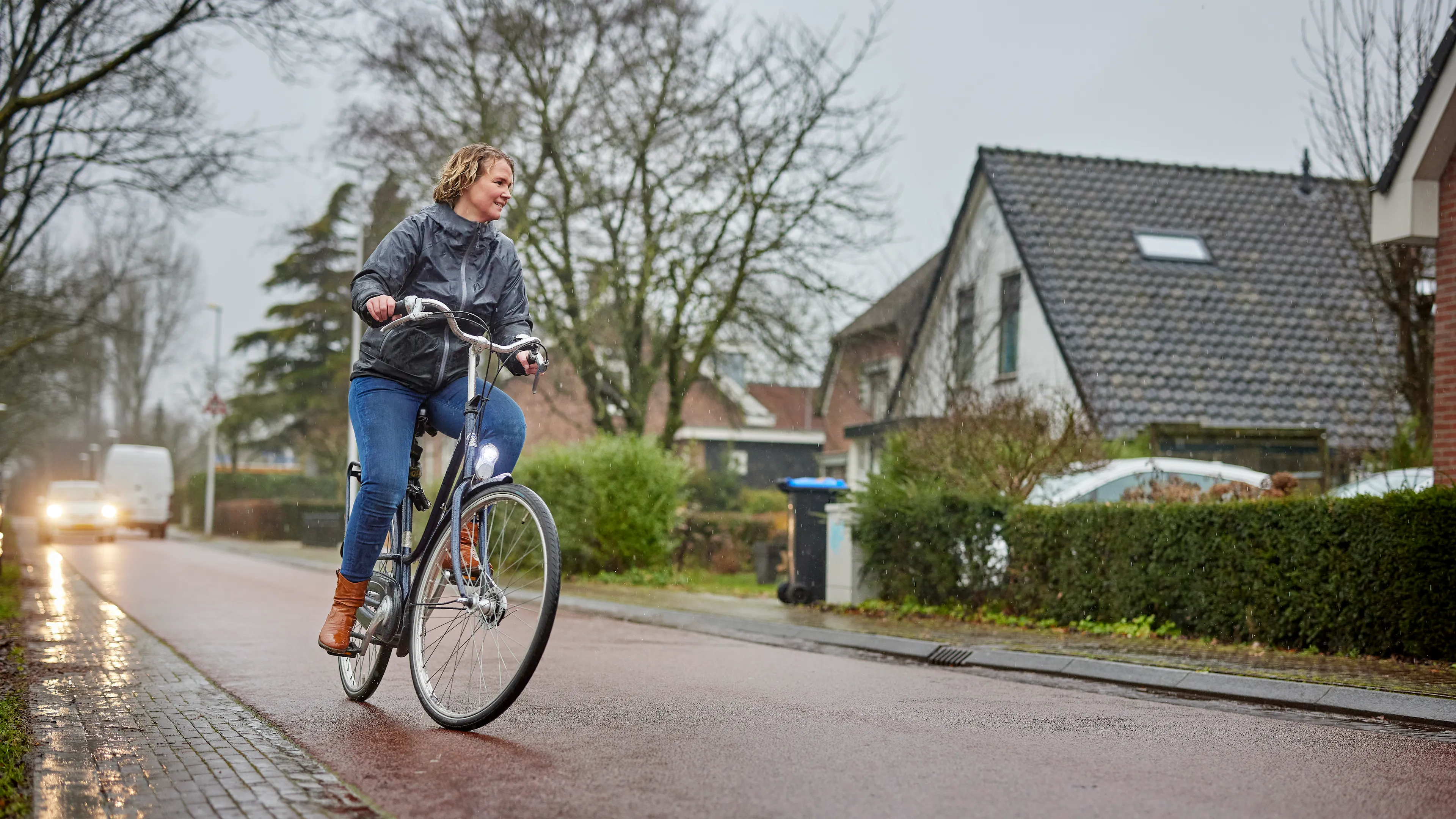 Vrouw fietst in de regen door een woonwijk