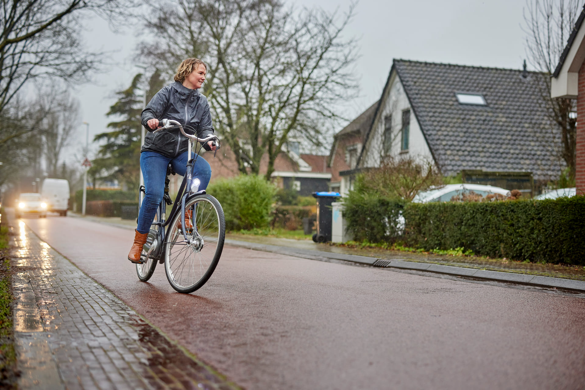 Vrouw fietst in de regen door een woonwijk