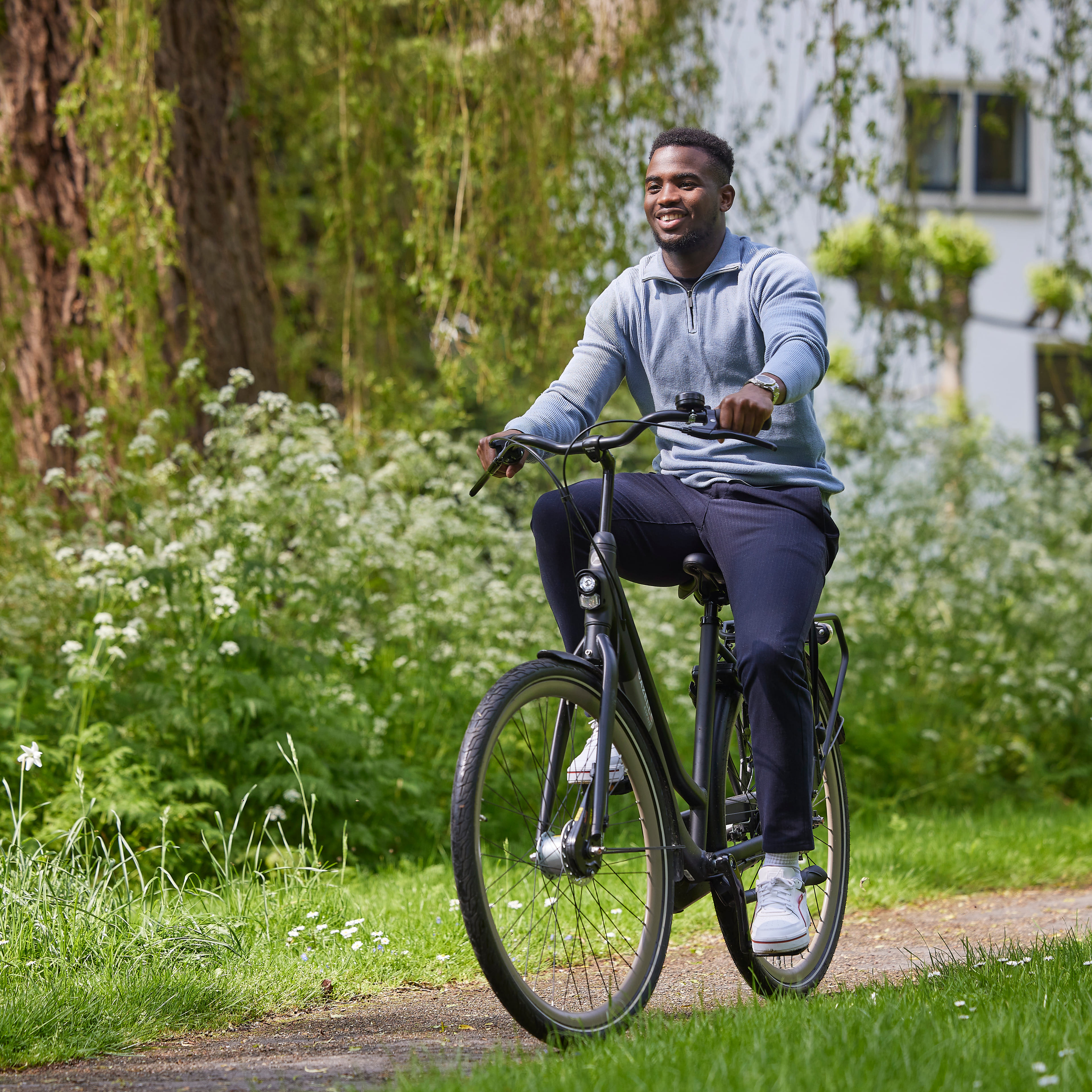 Een man op de fiets. Hij fietst door een park.