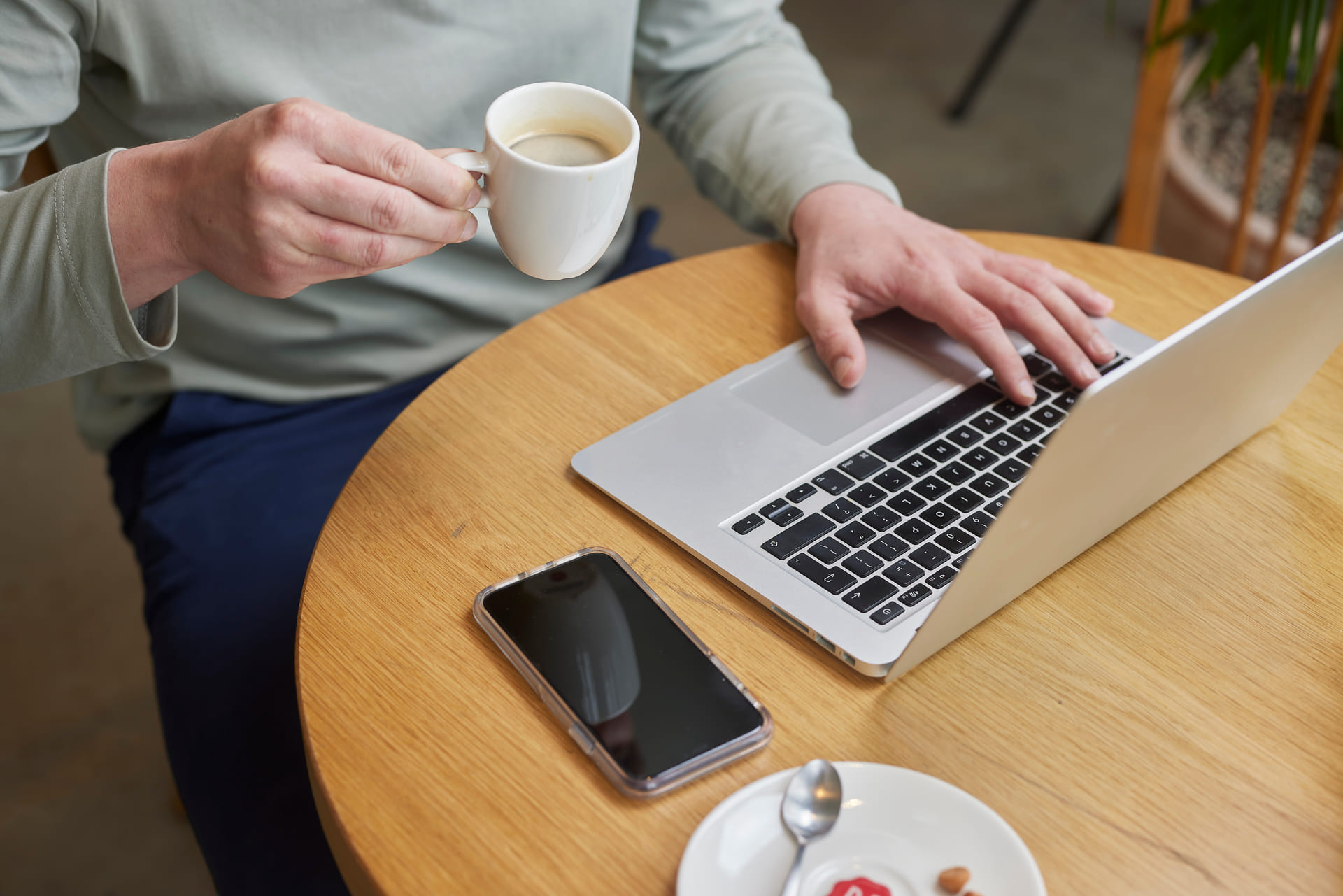 Een werknemer zit achter zijn laptop, terwijl hij een kop koffie drinkt.