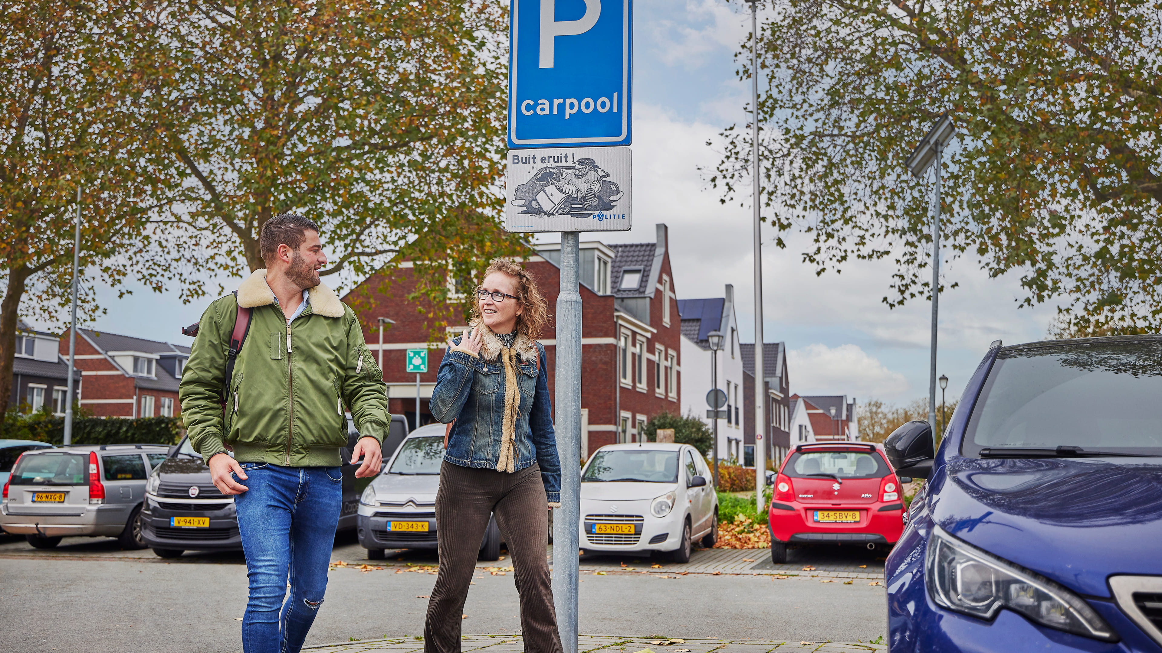 Een vrouw en een man lopen over een carpoolparkeerplaats richting een deelauto.