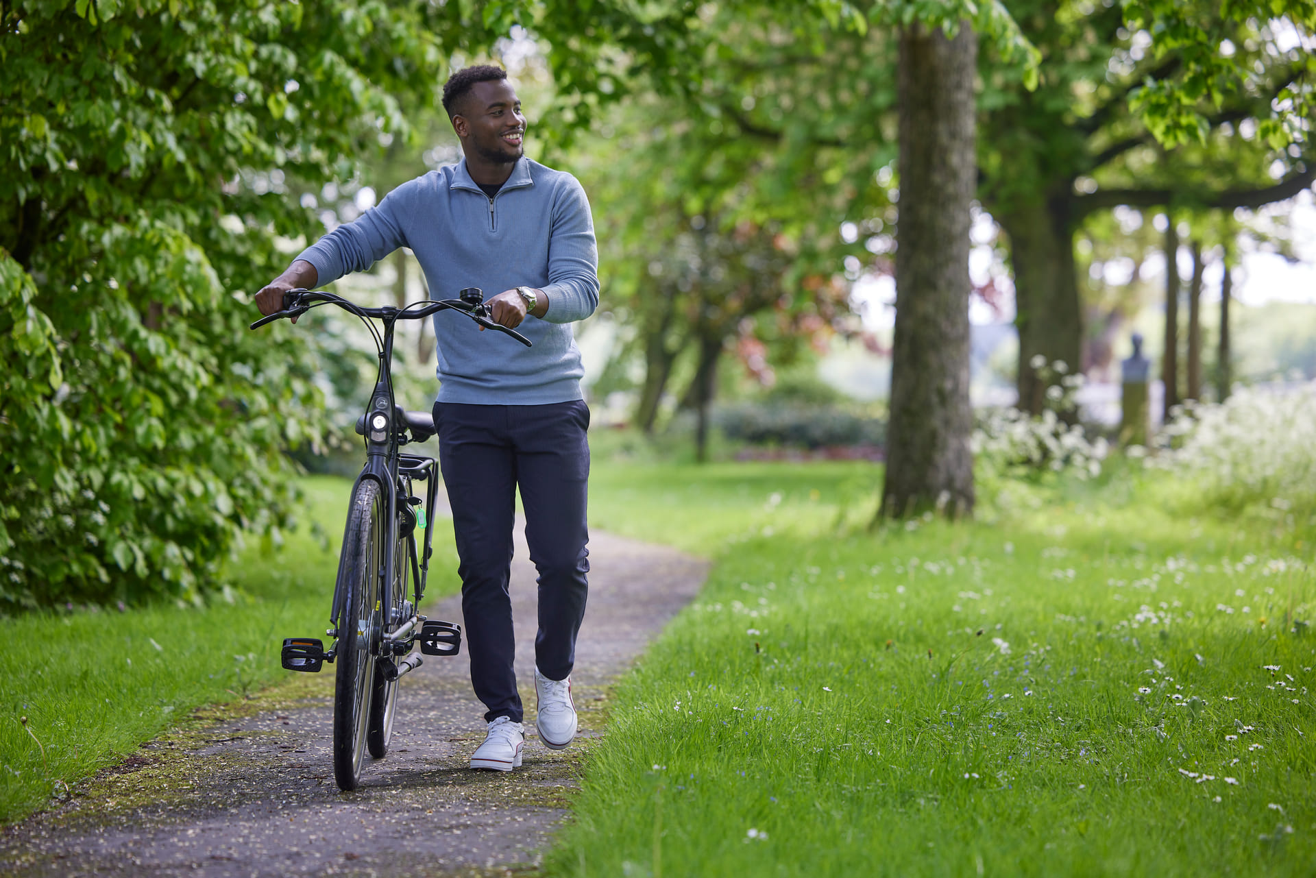 Man loopt met zijn fiets aan de hand door een park.